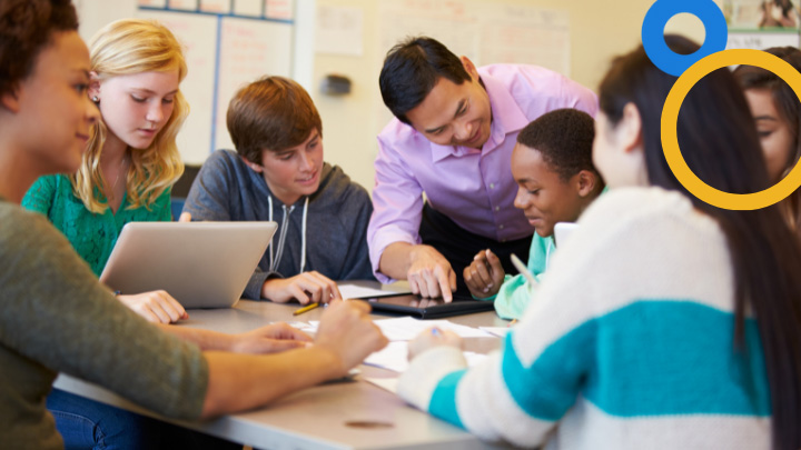 Teacher helping high school students with laptop and tablet